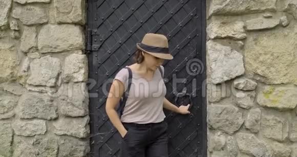 女游客戴着帽子背着背包从中世纪石堡的金属古门走过来视频的预览图