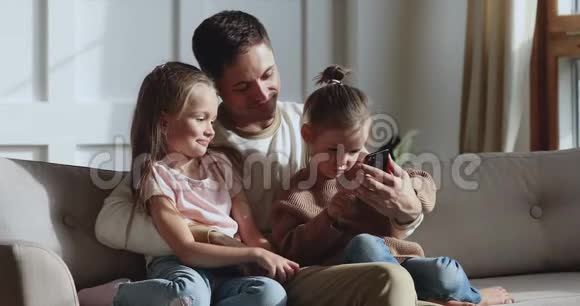 可爱的小女儿学习使用智能手机与家人放松视频的预览图
