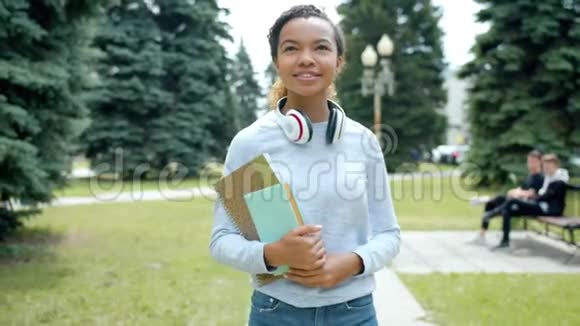 美丽的非裔美国女孩在公园里散步手里拿着书微笑视频的预览图
