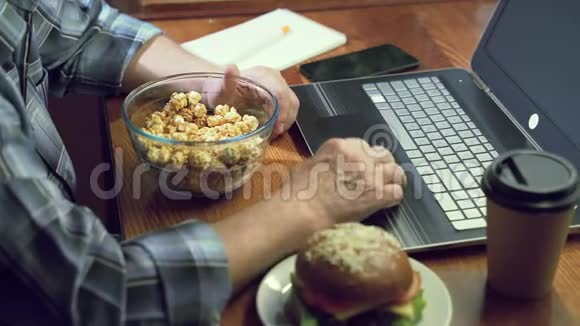 一位老人在家看电影或在笔记本电脑上工作时手拿一碗爆米花的特写镜头视频的预览图