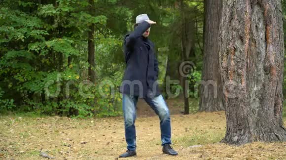 一个戴着帽子和外套的商人在树林里愉快地跳舞抚摸着帽子视频的预览图