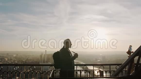 年轻快乐的游客带着相机和背包在埃菲尔铁塔慢动作顶部拍摄史诗般的巴黎日落视频的预览图