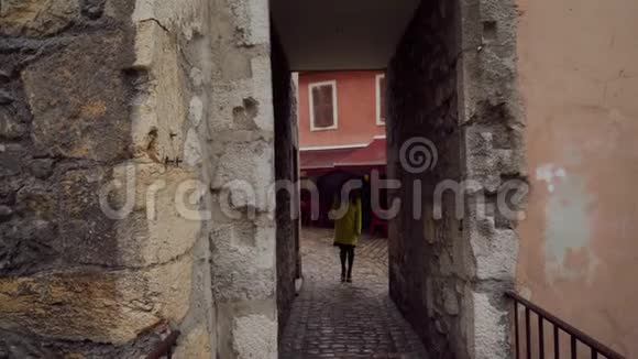 年轻的黑发女孩穿着黄色外套带着雨伞走在法国安纳西老城区狭窄的鹅卵石街道上视频的预览图