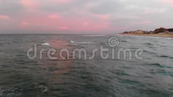空中观看无人机镜头低飞行在一个废弃的海滩上日落带着滚滚波浪和粉红云彩的沙滩视频的预览图