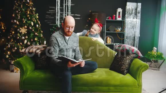 圣诞节概念一个戴眼镜的爸爸在看书他的女儿需要注意视频的预览图