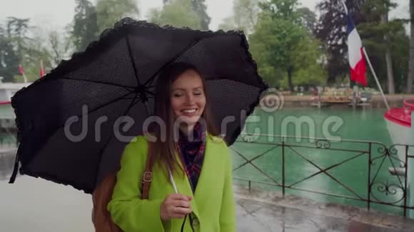 穿着黄色外套的漂亮女孩站在雨中拧着一把可爱的黑色雨伞微笑着调情法国安纳西湖视频的预览图