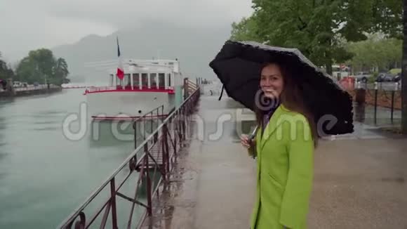 快乐的女人穿着黄色外套带着黑色圆点伞沿着风景优美的法国安纳西湖漫步在雨中后视图视频的预览图