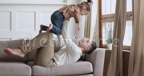 可爱的爸爸举起可爱的小女儿在沙发上玩耍视频的预览图