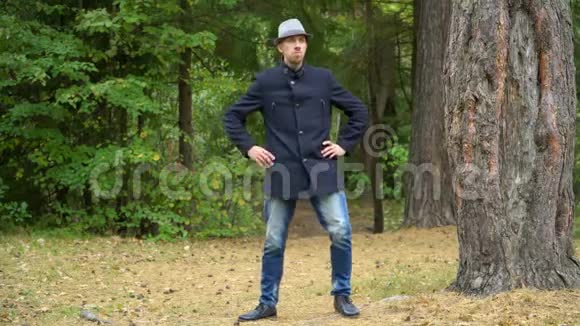 一个戴着帽子和外套的商人在树林里快乐地转动着他的手视频的预览图