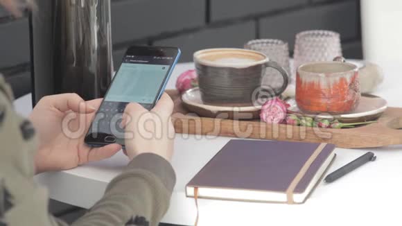 一个女孩拿着电话坐在一张白桌子旁端着两杯咖啡写着一条信息视频的预览图
