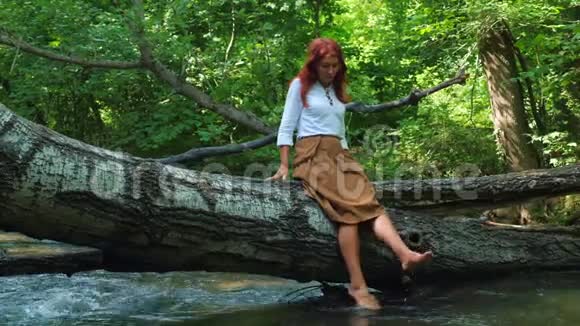女孩坐在树干上的河水中浇水视频的预览图