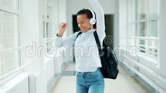 快乐的学生戴着耳机跳舞唱着享受学校大厅的音乐视频的预览图