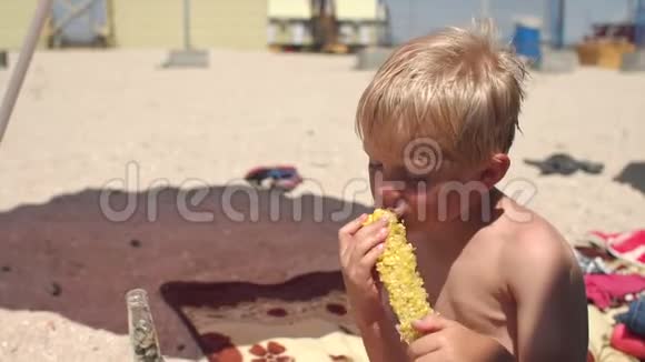 夏天在炎热的天气里小金发男孩在海滩上吃甜玉米视频的预览图