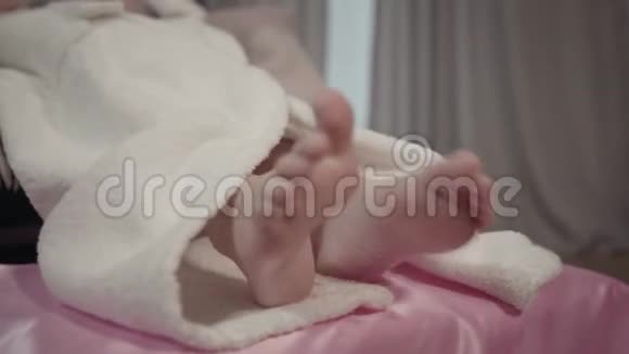 穿着白色浴袍躺在粉红色床上的白种人小女孩的特写双脚洗澡后的孩子在她的房间里休息视频的预览图