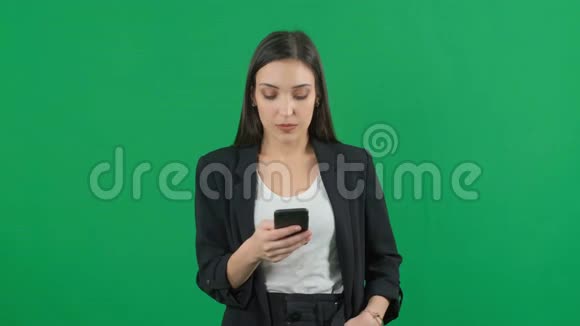 漂亮的欧洲女商人西装革履在彩色绿色屏幕背景上使用智能手机视频的预览图