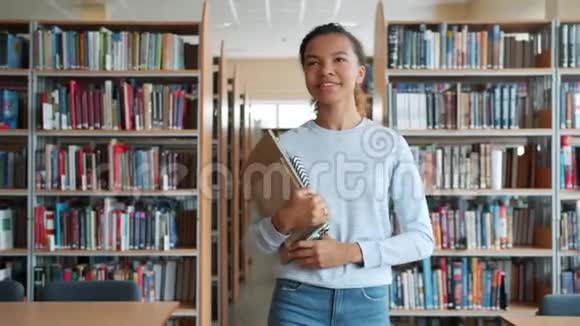 快乐的少女带着书走在高中图书馆微笑视频的预览图