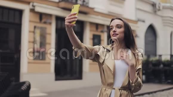 美丽的快乐女孩视频通话保持电话垂直微笑交谈和手势站在城市视频的预览图