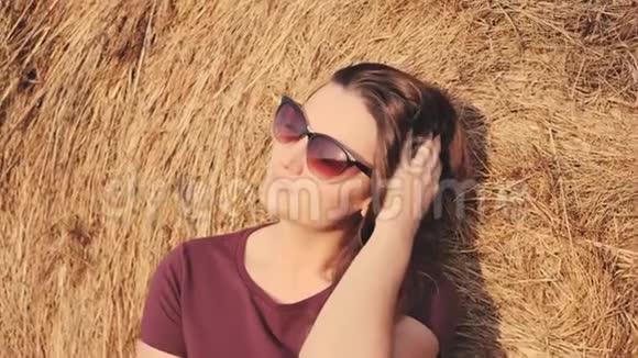 一个女人坐在干草堆旁边的田野里享受着新鲜的农村空气肖像视频的预览图