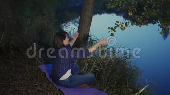 女人坐在瑜伽垫上晚上在河边冥想视频的预览图