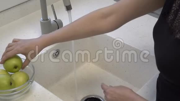 一个成年女孩在厨房的水槽里的水流下洗着漂亮的绿色苹果然后把它们放在一个黑色的盘子里视频的预览图