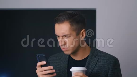 专注和皱眉的男性企业家喝咖啡并使用智能手机在办公室咖啡休息视频的预览图