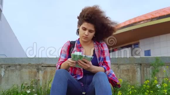 一个留着非洲发型的少女坐在草坪或城市街道上的公园里数着欧元视频的预览图