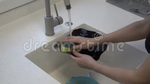特写女人手在厨房水槽里的一股水流下用黄色的海绵洗一个黑色的盘子家庭作业视频的预览图