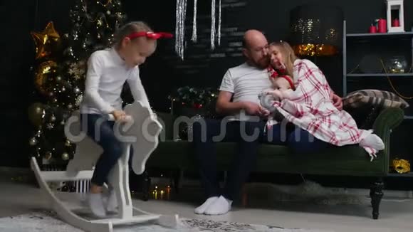 新年一家人坐在沙发上的毯子下旁边的女儿骑着一匹玩具马视频的预览图