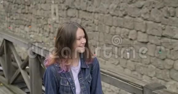 穿着牛仔夹克的紫发少女微笑着走在老旅游小镇上视频的预览图