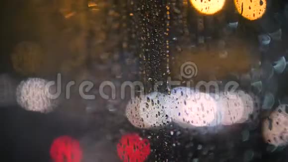雨天公交车车窗玻璃上的雨水滴落以模糊的夜间城市交通为背景4K视频的预览图