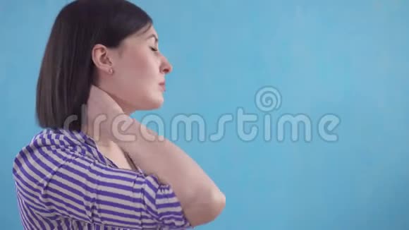 年轻女子戴着保护项圈以防止站在蓝色背景上的颈部疼痛视频的预览图