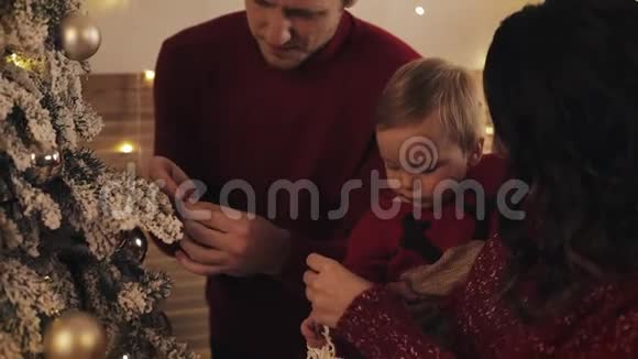 一家人带着小男孩在他们明亮舒适的客厅装饰圣诞树看着幸福的微笑女人生孩子视频的预览图