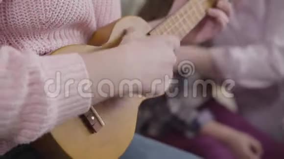 女性白种人的双手特写弹奏四弦琴穿着粉红色毛衣的年轻女人在家休息爱好生活方式音乐视频的预览图