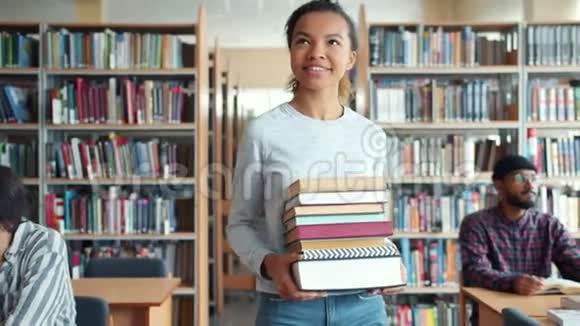 带着书走在图书馆微笑的混血女学生视频的预览图