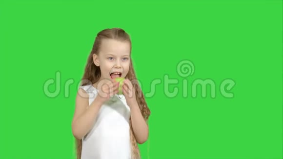一个小女孩在绿色屏幕上吃绿色苹果的肖像色度键视频的预览图