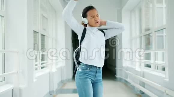 戴着耳机的快乐女孩在大学大厅唱歌跳舞视频的预览图