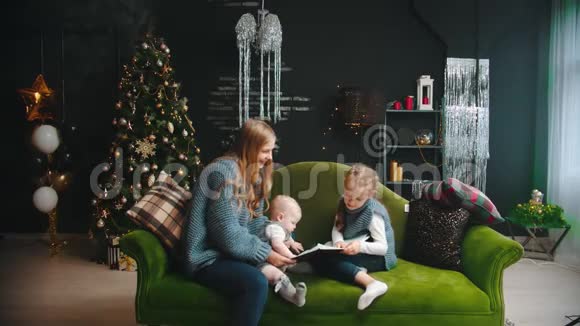 圣诞节的概念一个妈妈和她的孩子坐在沙发上爸爸来给他们带来礼物视频的预览图