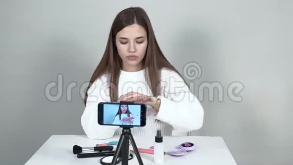 手机前的女博主在她的手上涂了奶油布置化妆品视频的预览图