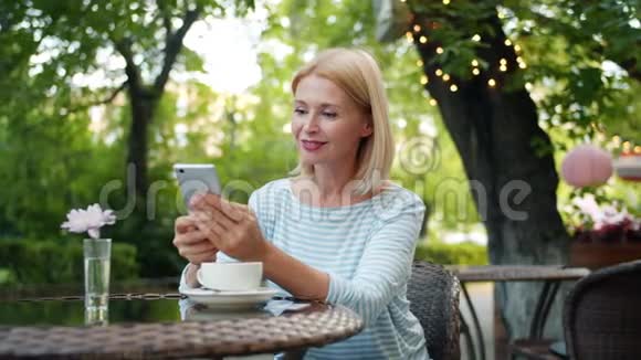 漂亮的成熟女士在街头咖啡馆享受智能手机触摸屏幕视频的预览图