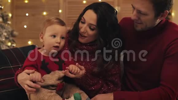 年轻漂亮的妈妈英俊的爸爸可爱的笑脸娃娃坐在沙发上的一家人视频的预览图