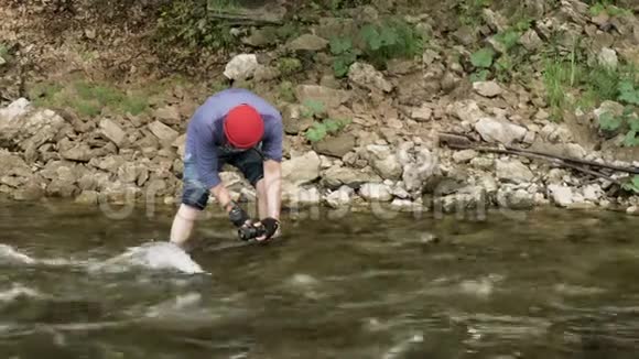 一个人拿着相机站在一条岩石河里为水面拍照库存录像男性徒步旅行者视频的预览图