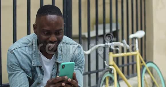 性格开朗的非裔美国年轻人用智能手机输入短信坐在附近时看上去既兴奋又欢笑视频的预览图