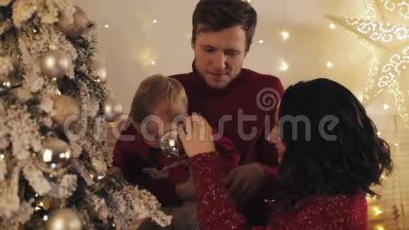 爸爸妈妈和宝宝幸福的一家人站在家中的圣诞树旁爸爸抱着小男孩亲吻他视频的预览图