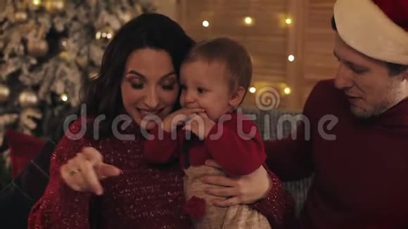 幸福的微笑年轻家庭与小孩子穿着冬季毛衣坐在圣诞树背景在科西视频的预览图