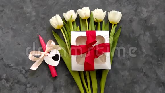 白色郁金香花银色礼盒红色丝带蝴蝶结和蜡烛在黑暗背景平躺4K顶部视图浪漫爱情视频的预览图