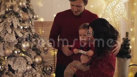 幸福的微笑家庭与小宝宝站在圣诞树附近舒适的客厅妈妈抱和拥抱宝宝丈夫视频的预览图