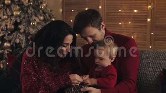 在温暖舒适的家居氛围中带着孩子的年轻家庭在靠近圣诞树的沙发上寻找快乐的小窝视频的预览图