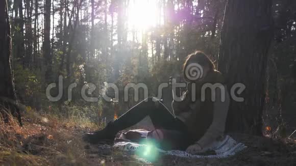 快乐的年轻女子游客喝着热茶吃着饼干在秋天的森林里享受阳光女性旅行者享受视频的预览图
