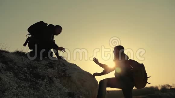 在日落的背景下游客们爬上山崖的剪影互相帮助手提供帮助视频的预览图