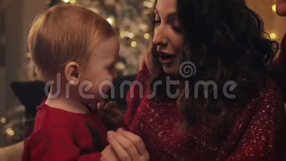 小可爱微笑的小男孩跳着妈妈跪着爸爸坐在他们旁边的背景圣诞树视频的预览图